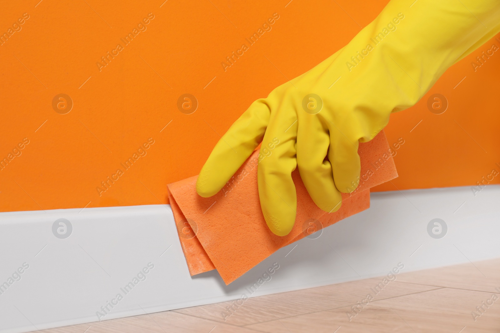 Photo of Woman in protective glove cleaning plinth with sponge cloth indoors, closeup