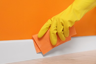 Photo of Woman in protective glove cleaning plinth with sponge cloth indoors, closeup