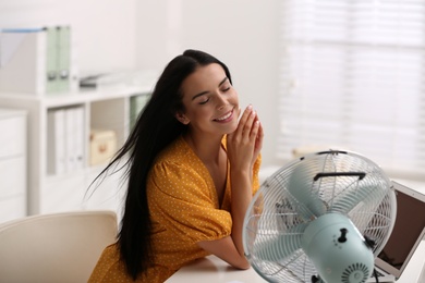 Photo of Young woman enjoying air flow from fan at workplace