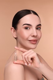 Beautiful young woman holding skincare ampoule on beige background