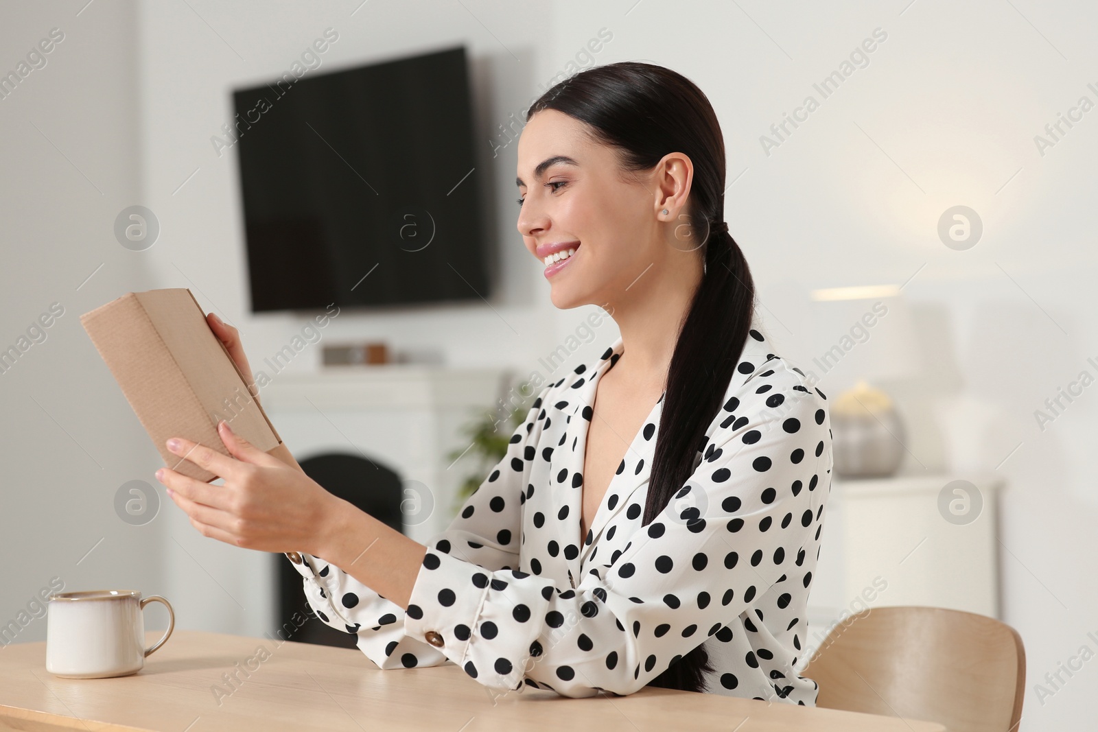 Photo of Happy young woman with parcel at table indoors. Internet shopping