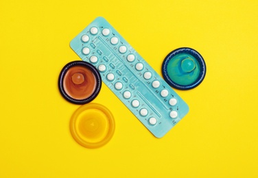 Photo of Condoms and birth control pills on yellow background, flat lay. Safe sex concept
