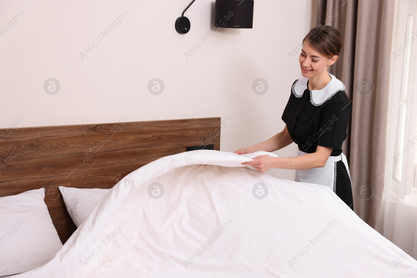 Photo of Beautiful chambermaid making bed in hotel room