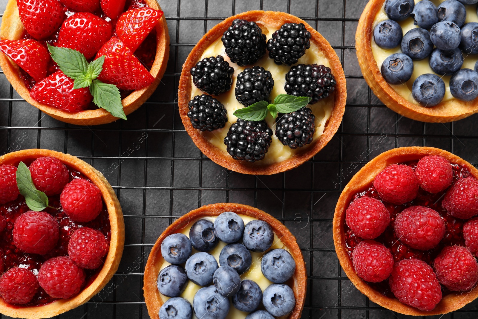 Photo of Tartlets with different fresh berries on grey table, flat lay. Delicious dessert