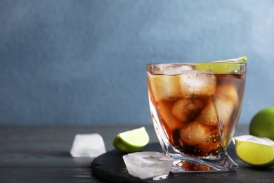 Glass of cocktail with cola, ice and cut lime on table. Space for text