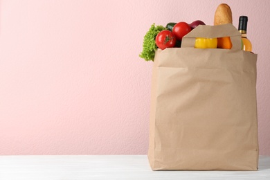 Photo of Shopping paper bag with different groceries on table against pink background. Space for text