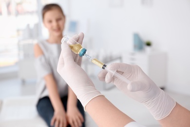 Doctor filling syringe with medicine and child on background. Vaccination day