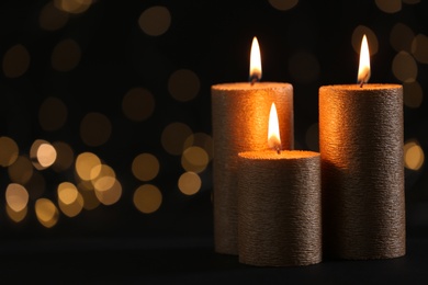 Burning gold candles against blurred lights in darkness. Space for text