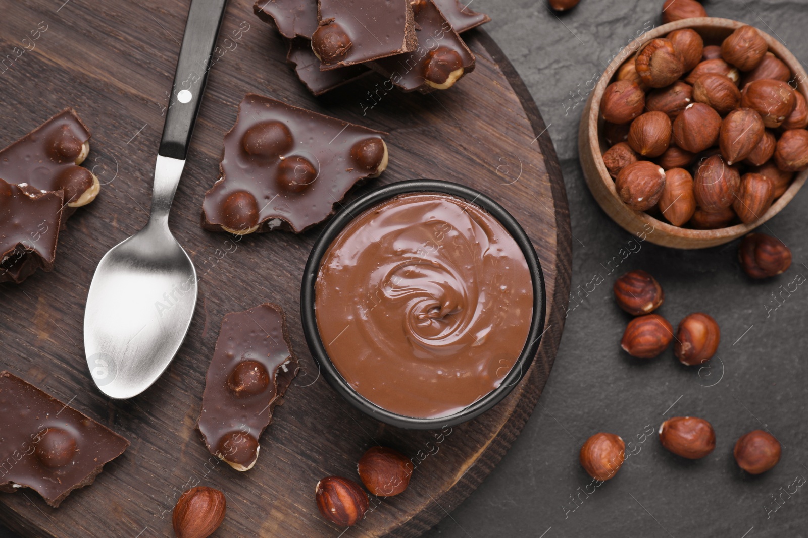 Photo of Bowl with tasty paste, chocolate pieces and nuts on grey table, flat lay