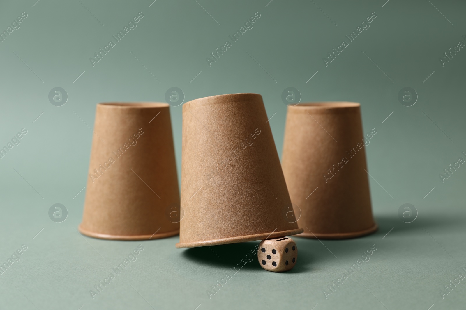 Photo of Three paper cups and dice on pale olive background. Thimblerig game