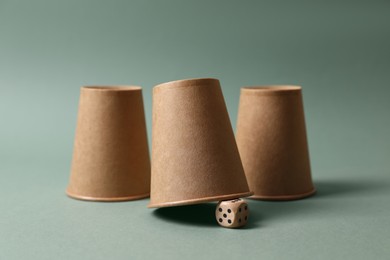 Photo of Three paper cups and dice on pale olive background. Thimblerig game