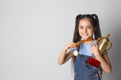 Photo of Happy girl with golden winning cup and medal on light background. Space for text
