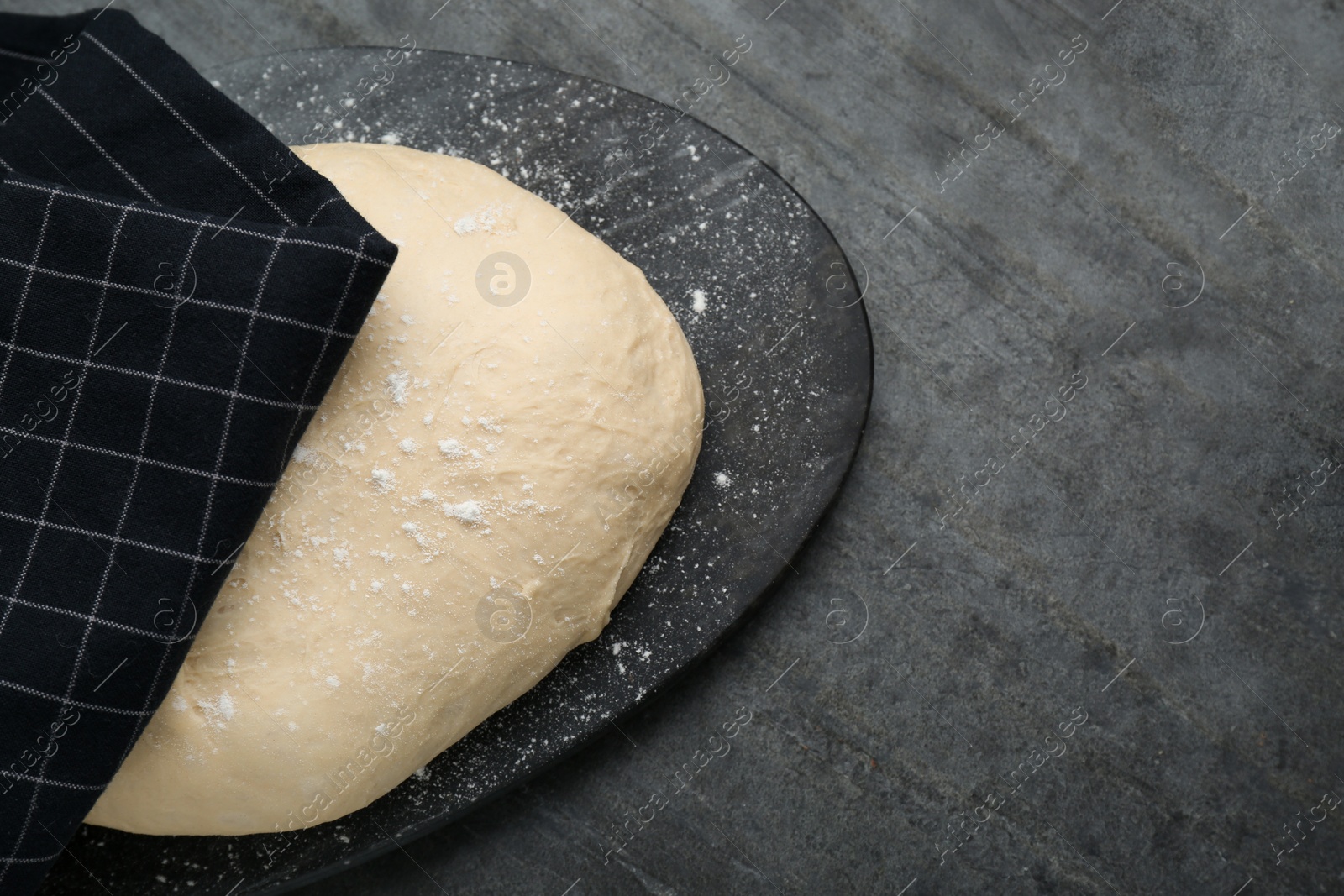 Photo of Fresh yeast dough with flour on black table, top view. Space for text