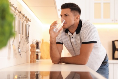 Man drinking glass of pure water at countertop in kitchen