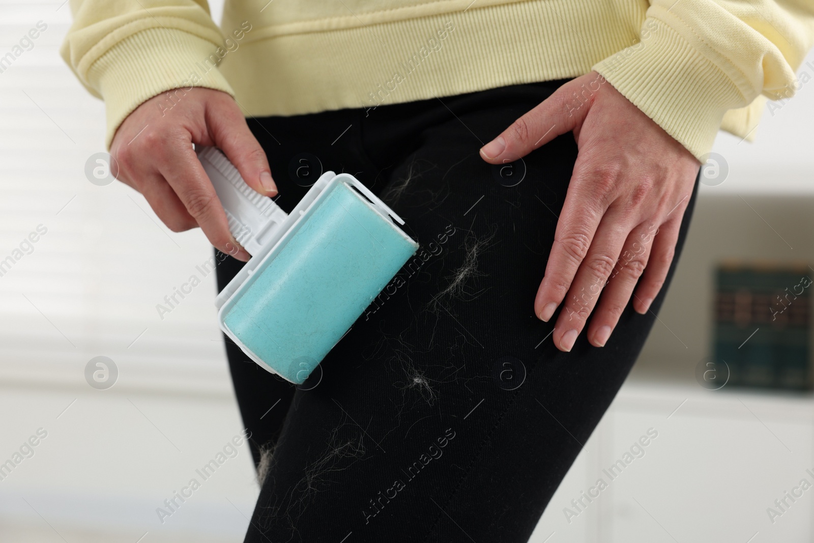 Photo of Woman with lint roller removing pet hair from black trousers indoors, closeup