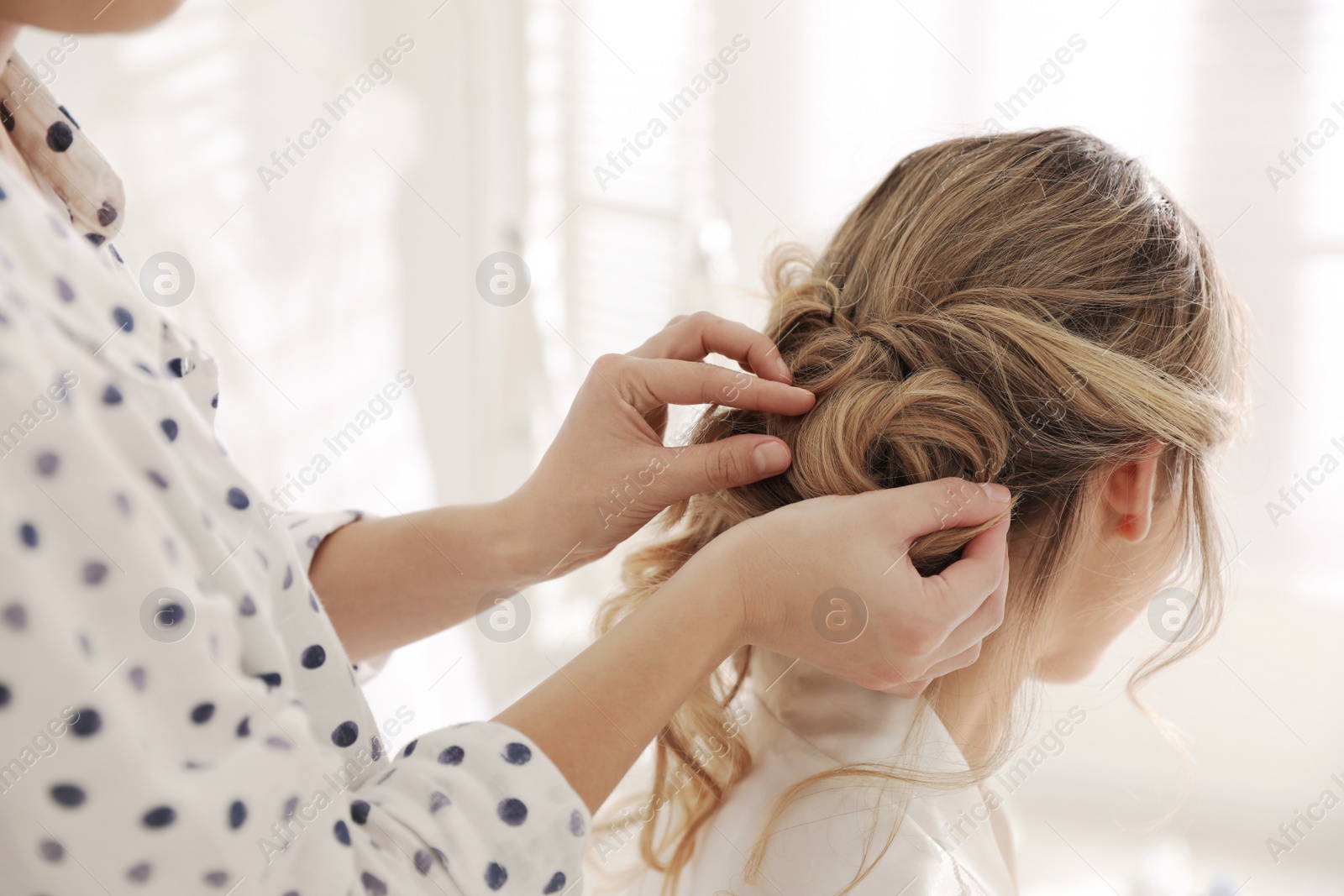 Photo of Professional stylist making wedding hairstyle for bride in salon, back view