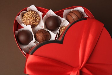 Photo of Heart shaped box with delicious chocolate candies on brown background, closeup