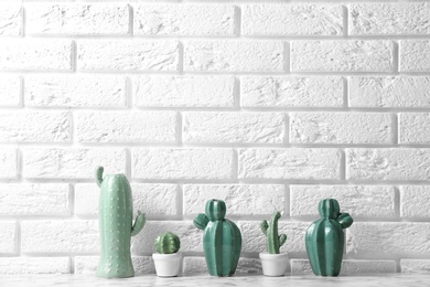 Decorative cacti on table near brick wall, space for text. Interior decor