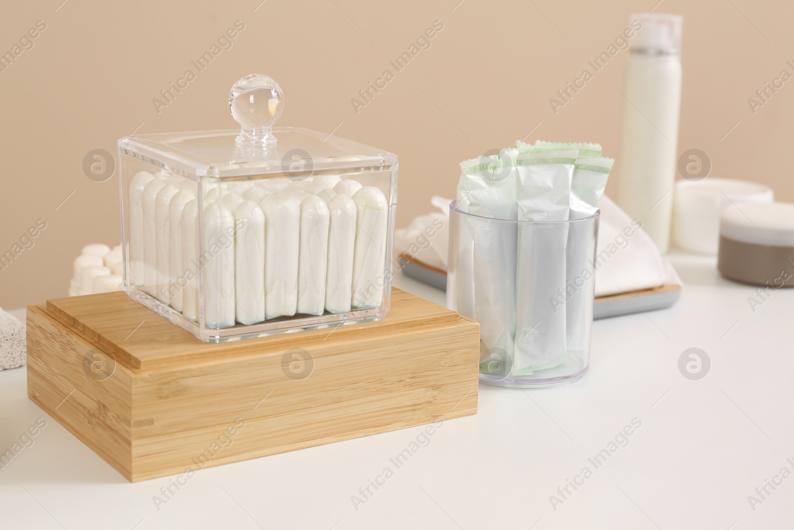 Photo of Many different tampons and personal care products on white table near beige wall