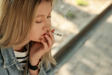 Young woman smoking cigarette outdoors, closeup. Space for text