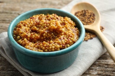 Fresh whole grain mustard in bowl on wooden table, closeup