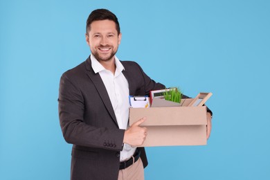 Photo of Happy unemployed man with box of personal office belongings on light blue background