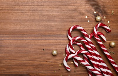 Photo of Sweet Christmas candy canes and festive decor on wooden table, flat lay. Space for text