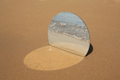 Round mirror reflecting sea on sandy beach