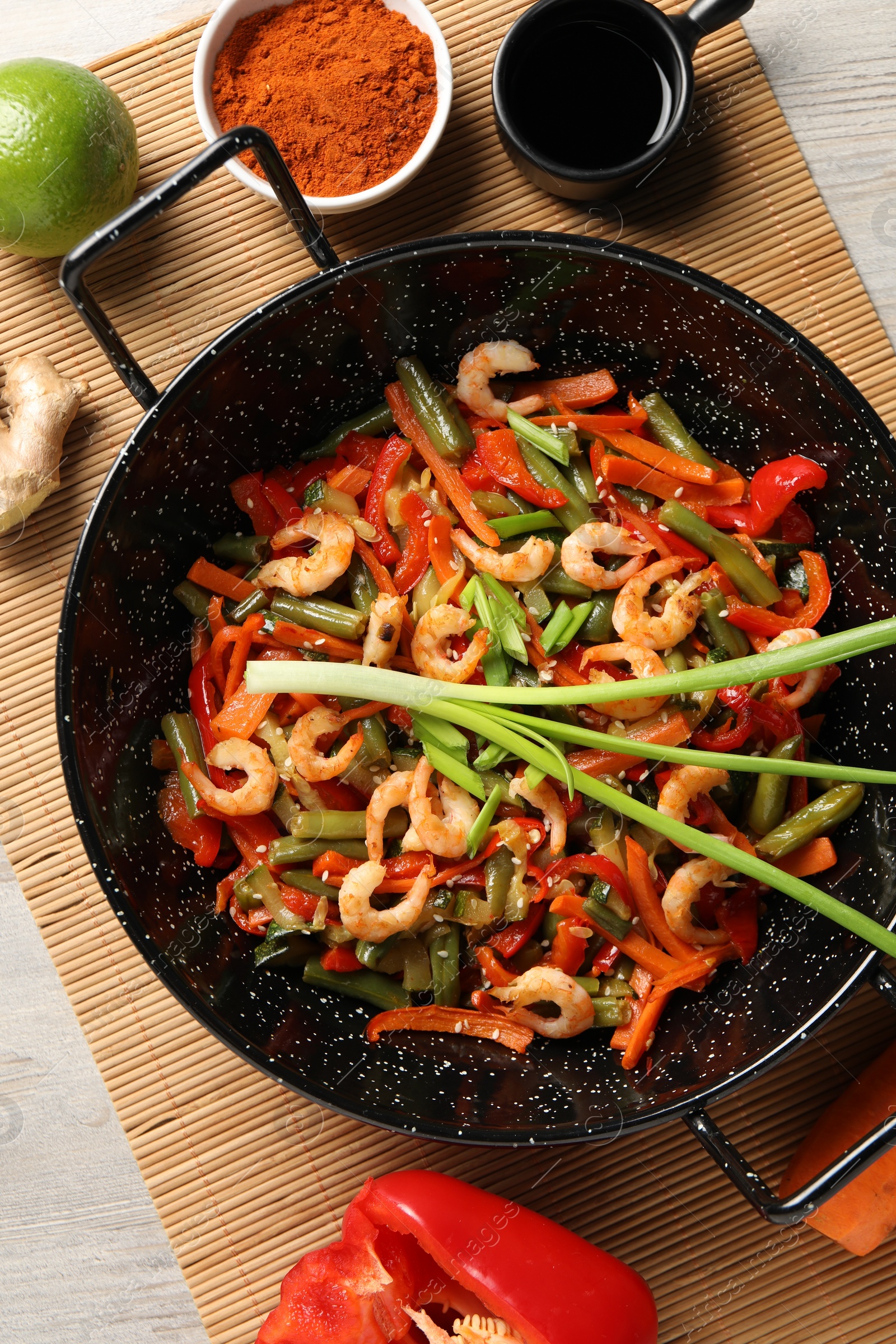 Photo of Shrimp stir fry with vegetables in wok and ingredients on wooden table, flat lay