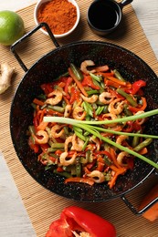 Shrimp stir fry with vegetables in wok and ingredients on wooden table, flat lay