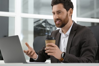 Man with cup of coffee working on laptop at white desk in office