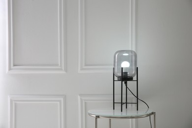 Photo of Table with modern lamp near white wall, space for text. Interior element