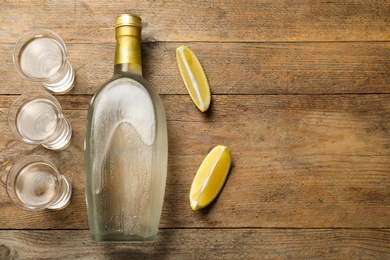 Photo of Bottle of vodka, lemon and shot glasses on wooden table, flat lay. Space for text