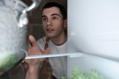 Photo of Man near refrigerator in kitchen at night, view from inside