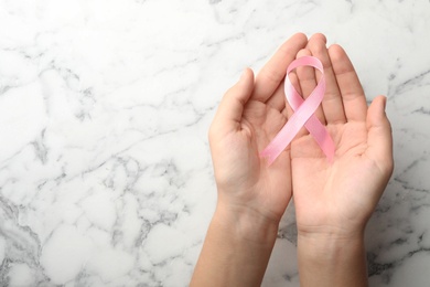 Woman holding pink ribbon on marble background, top view with space for text. Breast cancer awareness concept