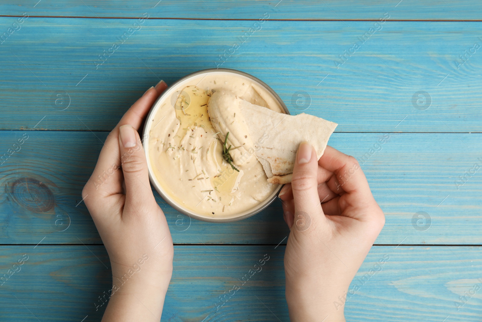 Photo of Woman dipping pita chip into hummus at turquoise wooden table, top view