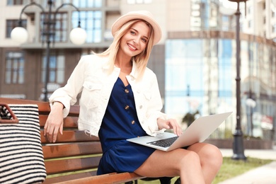 Photo of Beautiful woman using laptop on bench in city