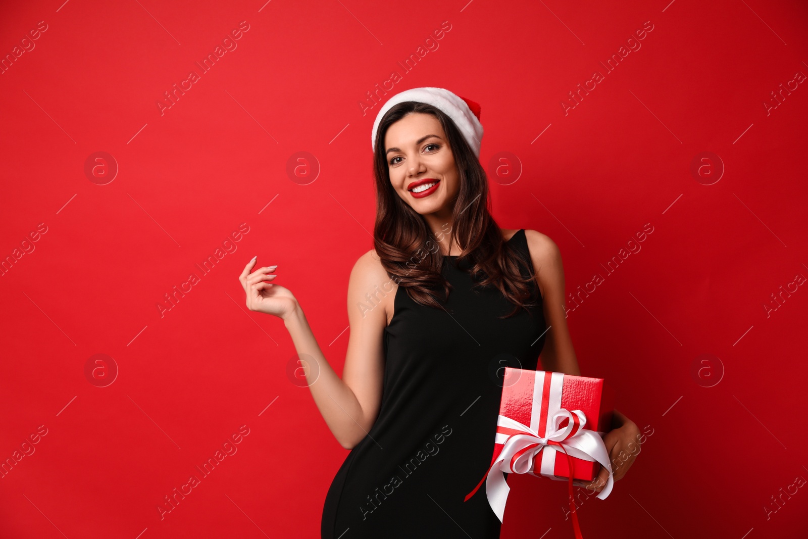 Photo of Beautiful woman wearing Santa hat with Christmas gift on red background