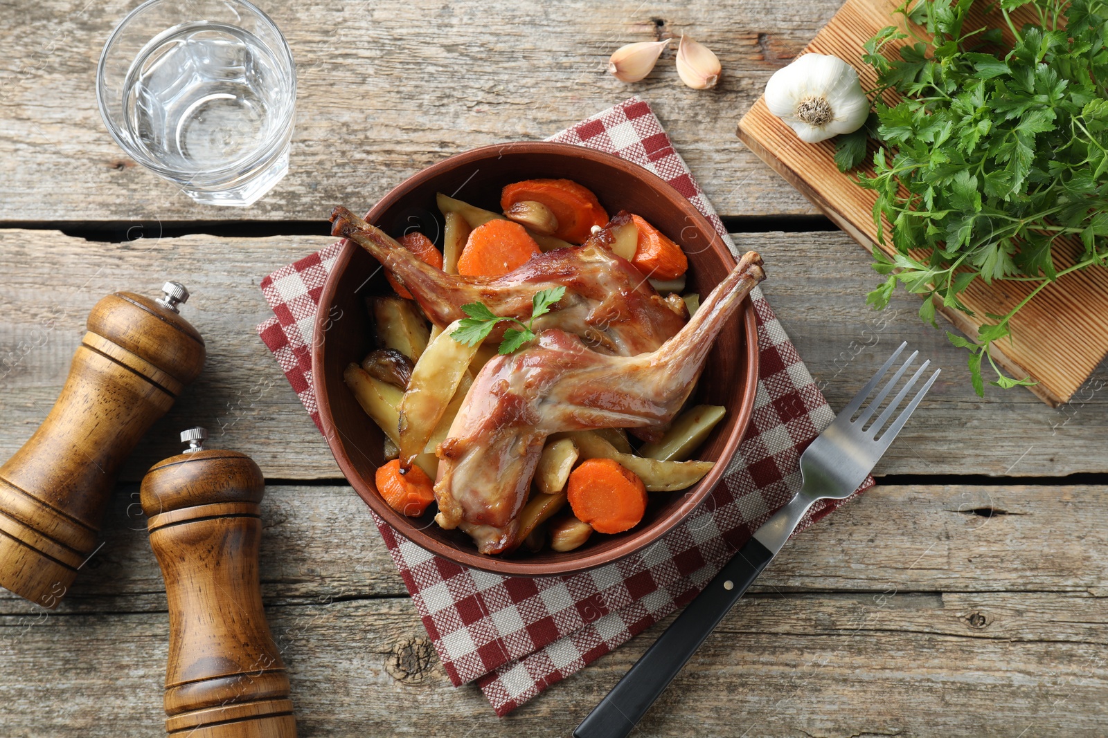 Photo of Tasty cooked rabbit with vegetables served on wooden table, flat lay