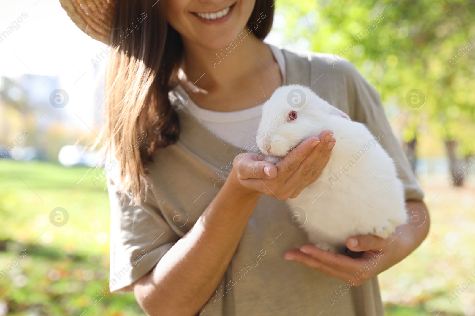 Photo of Happy woman holding cute white rabbit in park, closeup