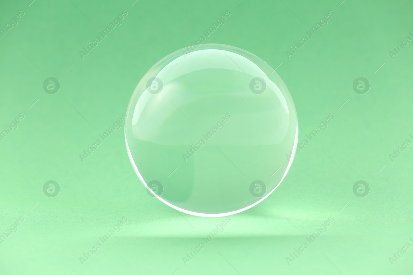 Photo of Transparent glass ball on light green background