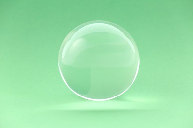 Photo of Transparent glass ball on light green background