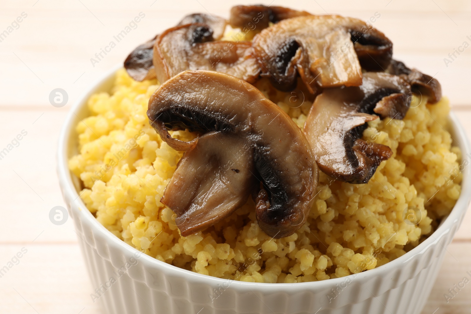 Photo of Tasty millet porridge and mushrooms in bowl on light wooden table, closeup