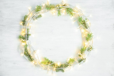 Photo of Glowing Christmas lights and fir branches on wooden background, top view