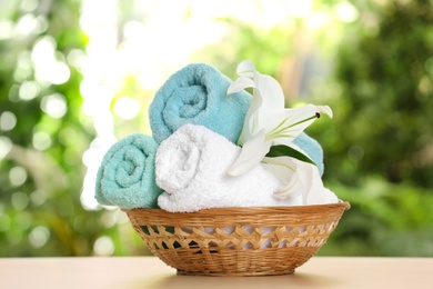 Photo of Basket with soft bath towels and flower on table against blurred background