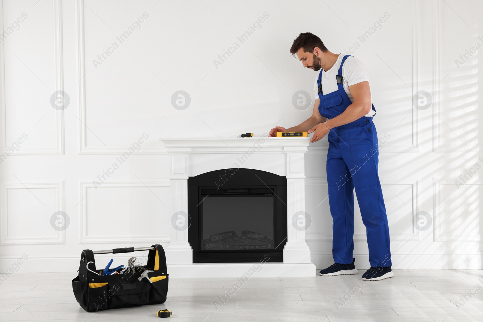 Photo of Professional technician using construction level for installing electric fireplace in room