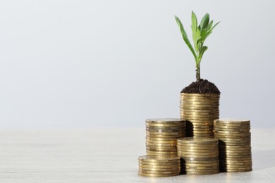 Stacks of coins with green seedling on white wooden table, space for text. Investment concept