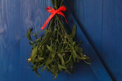 Photo of Mistletoe bunch with red bow hanging on blue wooden wall. Traditional Christmas decor