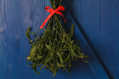 Mistletoe bunch with red bow hanging on blue wooden wall. Traditional Christmas decor