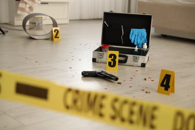 Photo of Crime scene markers, gun and criminologist case on floor in room